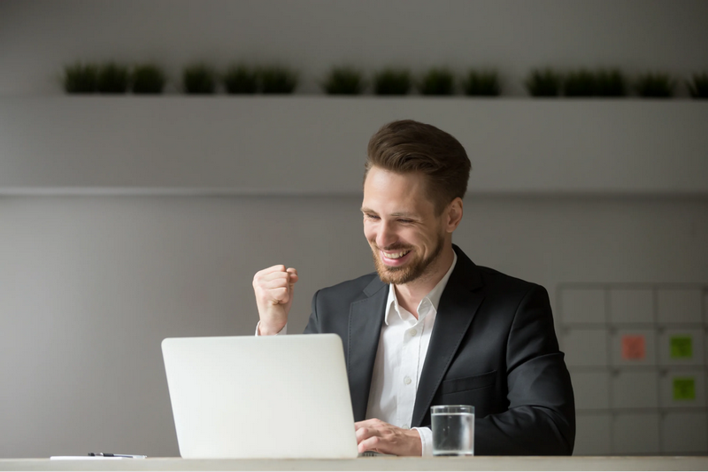 A man in a suit is celebrating while using a laptop.