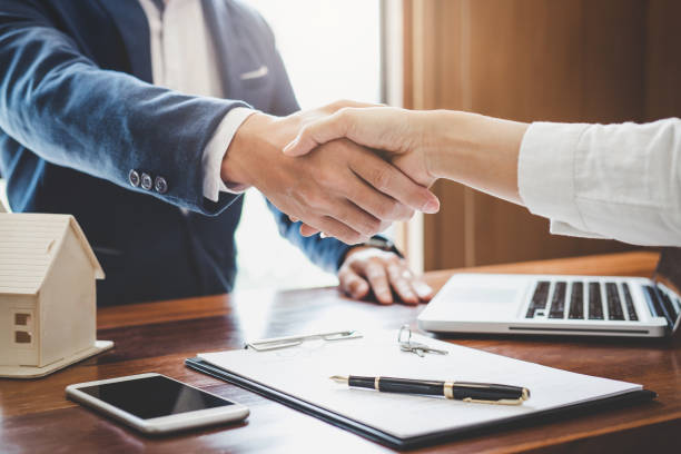 Two business professionals shaking hands over a desk with a laptop and documents, symbolizing trade agreements.