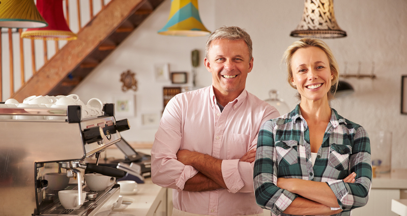 Two smiling people standing beside a coffee machine in a cozy café.