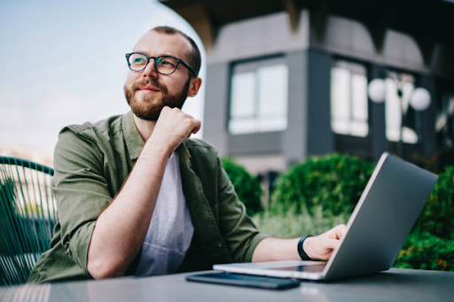 A man sits outdoors with a laptop, contemplating the application process for a Dubai residence visa.