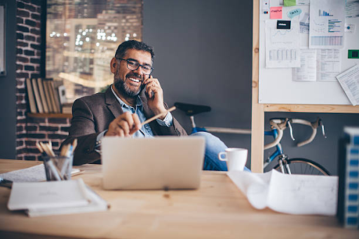 A man in an office on the phone, working on a laptop, planning a residence visa application for Dubai.